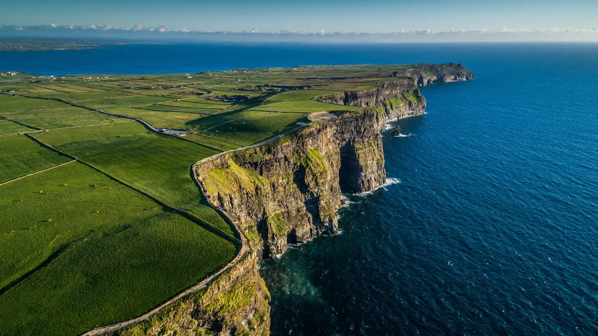 The Cliffs of Moher beside green fields on the Clare coast