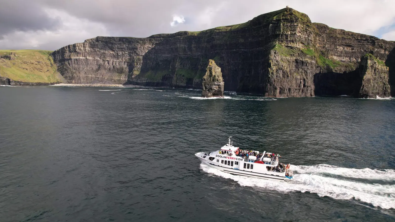 The Doolin ferry passing below the Cliffs of Moher with a sea stack behind